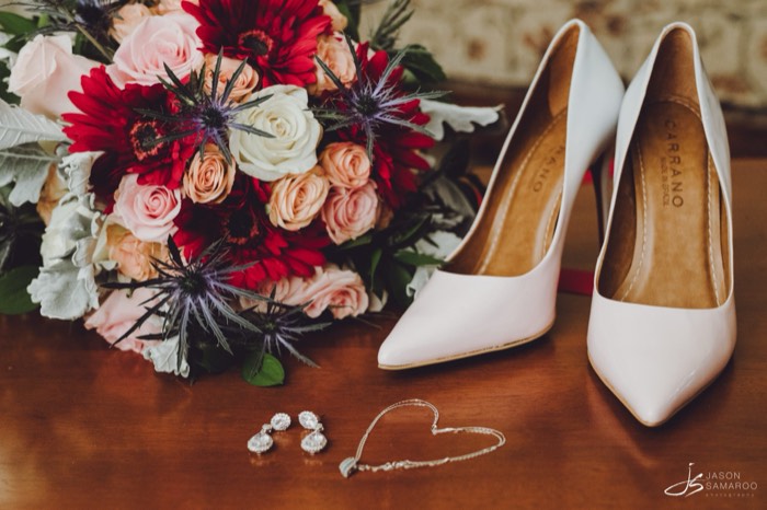 The bride's bouquet of red and blush roses beside her heels and earrings